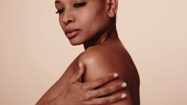 Serene woman with eyes closed, embracing herself against a neutral background, conveying self-love, confidence, and tranquility.