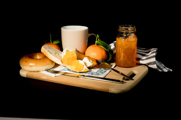 orange marmalade and cream cheese on a bagel on a wooden board on a black background