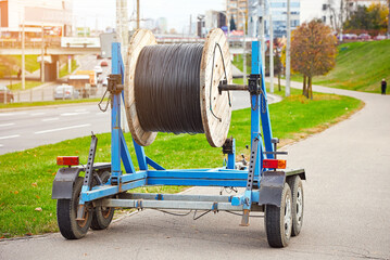 Deploying fiber optic cable. Laying optical cabling from wooden coil mounted on trailer. High-speed...