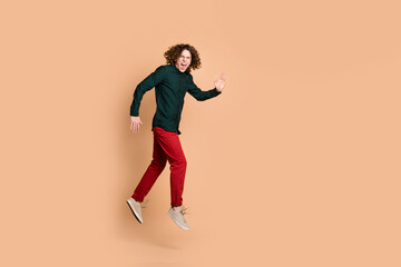 Fototapeta na wymiar Photo portrait of handsome young guy jump running hurry dressed stylish green garment isolated on beige color background