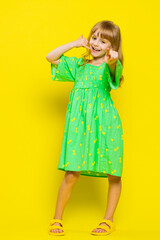 Call me, here is contact number. Blonde child girl kid looking at camera doing phone gesture like says hey you call me back advertising proposition. Preteen children on yellow background. Vertical