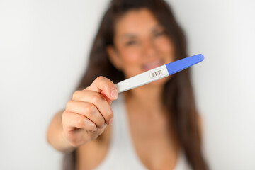Positive close-up pregnancy test held by happy woman out of focus. Motherhood concept
