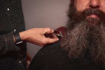 The barber's hand cutting the beard hair tips with a small razor