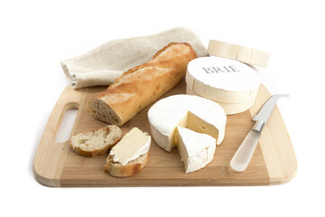 a round of brie or camembert cheese with a French baguette on a wooden board isolated on white