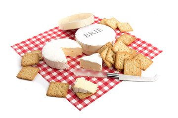 a round of brie cheese with a piece cut out with crackers on a red checked tablecloth