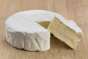 closeup of a round of brie cheese with a wedge cut out on a wooden table