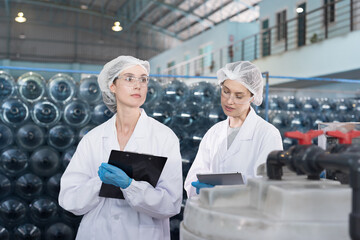 Two female worker inspecting quality of plastic drinking water tank in mineral water plant. Factory female worker working and checking plastic gallon during manufacturing water bottling process