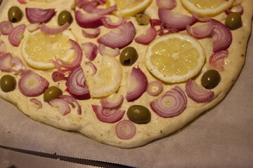 Close-up of ready to bake Focaccia with red onions, sliced lemons and green olives