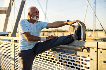 Senior bearded man in sportswear doing stretching before exercising on the bridge during sunset....