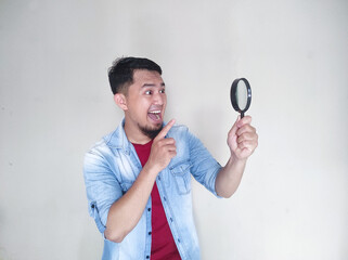 Asian man looking through magnifying glass with surprised expression