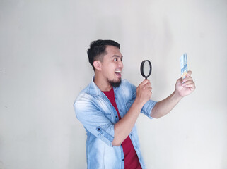 Asian mature man checking banknotes using magnifying glass with happy expression