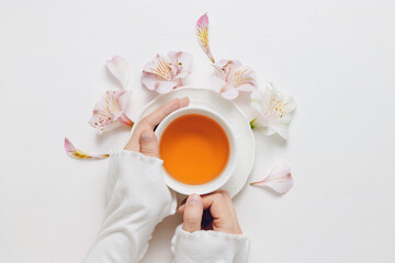 Woman hands hold cup of herbal tea with flowers on wooden table, top view. Healthy aromatic tea composition