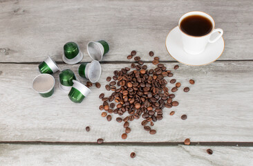 Coffee machine capsules, a cup of coffee and coffee beans lie on a wooden surface