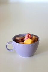 Purple cup filled with pastel macarons on white background. Selective focus.