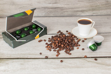 Coffee machine capsules in a package, a cup of coffee and coffee beans lie on a wooden surface