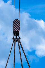 Detail shot of a hook of a crane with steel cables against a cloudy sky
