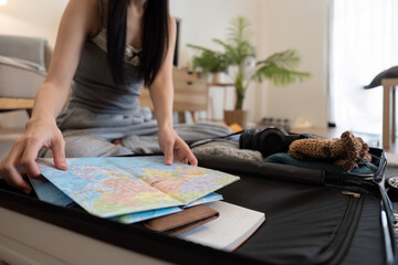 Asian woman packing suitcase or luggage and planning to travel on summer vacation on map