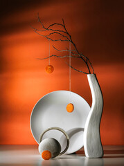Modern still life with a dry branch in a white vase and a carrot