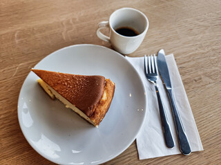 A slice of San Sebastian Cheesecake on a plate with a coffee in a cafe 