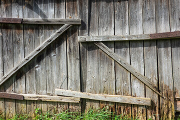 Old skewed closed barn gate. The gray wood is partially rotten. Rusty nails are visible. Background. Grunge.