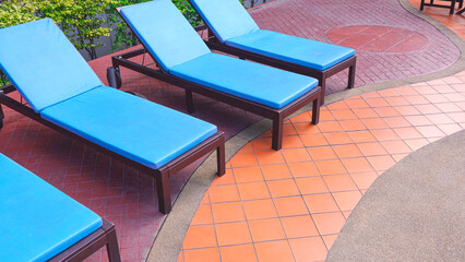 Row of blue sunbed lounger chairs on colorful curve lines pattern of stone tile floor decoration in poolside area at resort