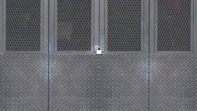 Black metal foldable entrance door background made from carbon steel diamond plate with grid wire mesh in industrial modern loft style, front view with copy space