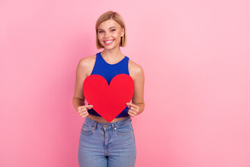 Photo of pretty young woman hold heart symbol empty space wear blue top isolated on pink color background