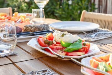 The warm glow of the evening sun enhances an appetizing plate of Caprese salad, complete with...