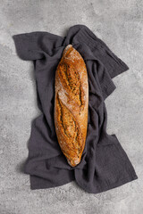 Rustic sourdough rye baguette with cereal on a towel on a gray table, top view