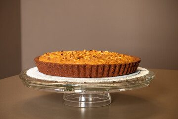 This inviting nut strewn pie, displayed on an elegant glass cake stand, features a perfectly baked,...