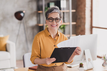 Photo of pretty retired woman cheerful smile read report dressed yellow formalwear modern workplace...
