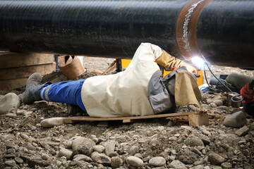 Close-up of a welder making a weld on a water pipe on a city street.