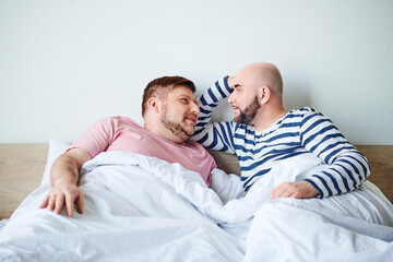 A pair of men laying side by side in bed, spending quality time together.