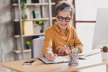 Photo of lovely mature lady signing documents sit table dressed yellow formalwear modern workplace success business owner home office