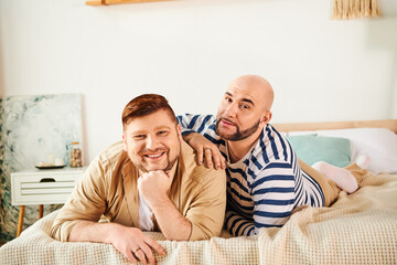 A couple of men enjoy a peaceful moment lounging on top of a bed.