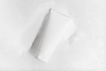 White mockup of a tube of cream in water with foam at an angle on a white background. Concept of gels and foams for washing face, moisturizer, cosmetics for beauty and self care. Image for your design