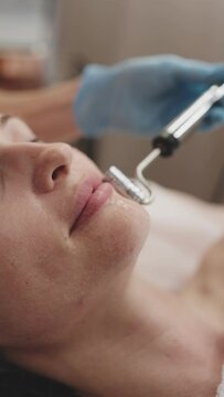 Professional cosmetologist performing microcurrent therapy on a woman's face for skin rejuvenation at a modern spa.