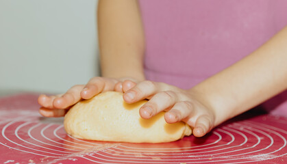 One girl bakes cookies, kneading the dough with her hands on the table.