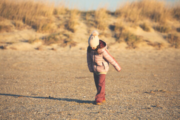 A child girl wearing the hat with a pompon strolling on the beach at sunset - 794138938