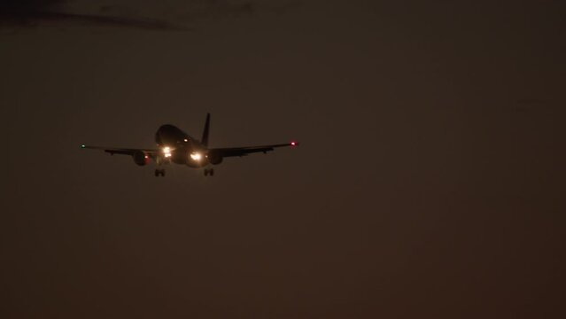 Airplane with bright landing lights approaches in a dark sky, wingtip navigation lights visible