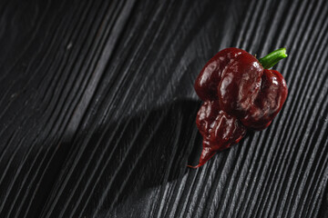 fresh brown extra hot carolina reaper chocolate pepper on black wooden rustic background