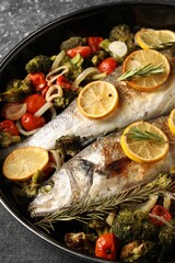 Baked fish with vegetables, rosemary and lemon on black textured table, above view