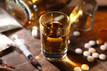 Alcohol and drug addiction. Whiskey in glass, syringes, pills and cocaine on wooden table, closeup