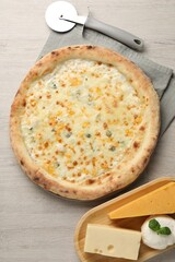 Delicious cheese pizza, cutter and different kinds of cheese on wooden table, flat lay