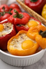 Delicious stuffed peppers with eggs in bowl on white table, closeup