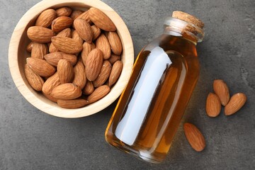 Almond oil in bottle and bowl with nuts on grey textured table, flat lay