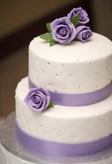 A white wedding cake with a quilted pattern and purple fondant roses on the top tier