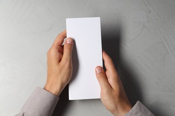 Man holding white blank card at light grey table, top view. Mockup for design
