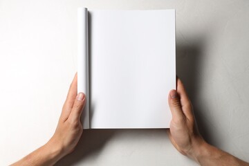 Man holding blank notebook at white table, top view. Mockup for design