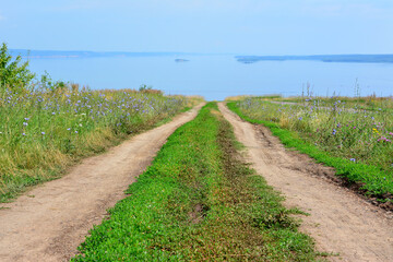 a dirt road is leading to a lake with a view of the water and a grassy field